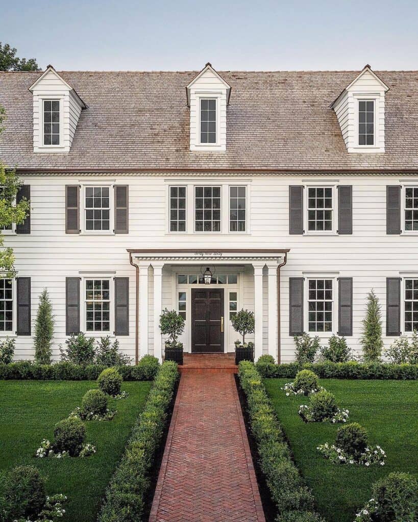 Elegant white colonial house with manicured garden and brick pathway leading to front door.
