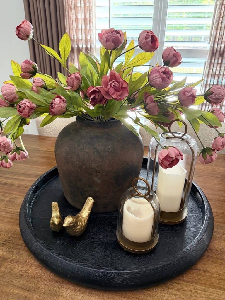 Beautiful pink tulip arrangement in a dark vase with candles on a tray.