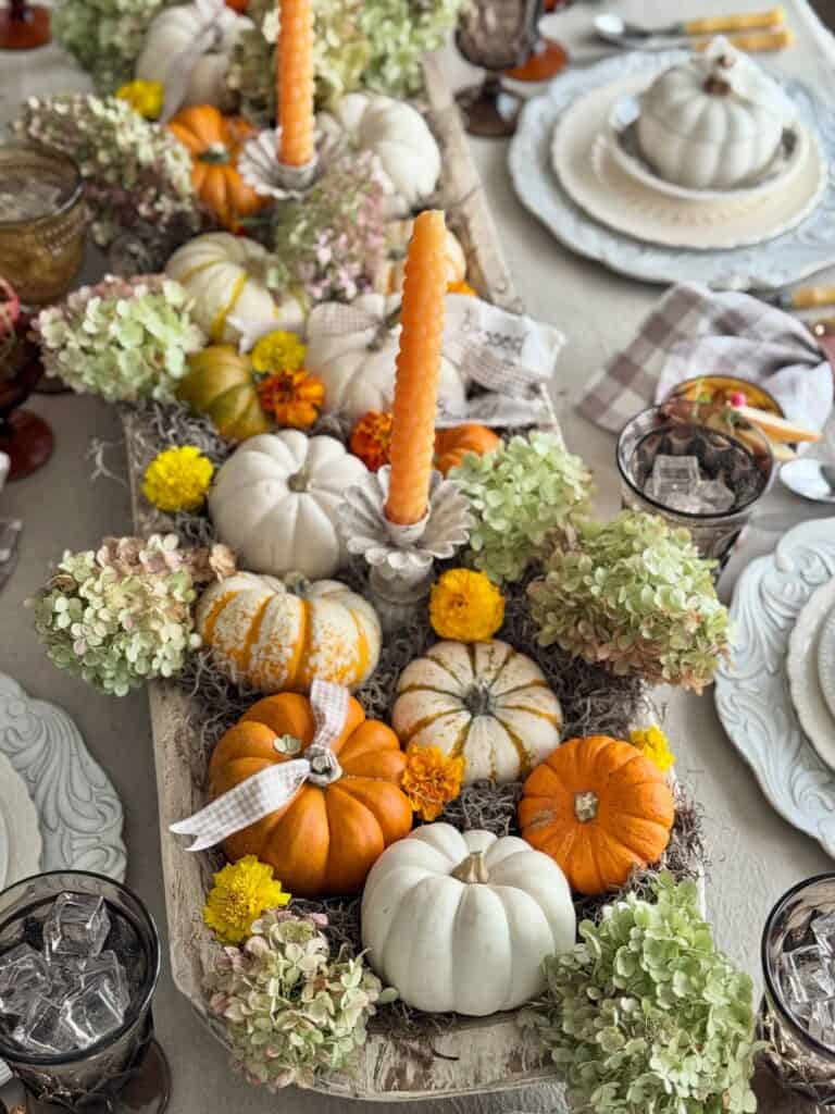 Fall-themed pumpkin centerpiece with candles and flowers for dining table decor.