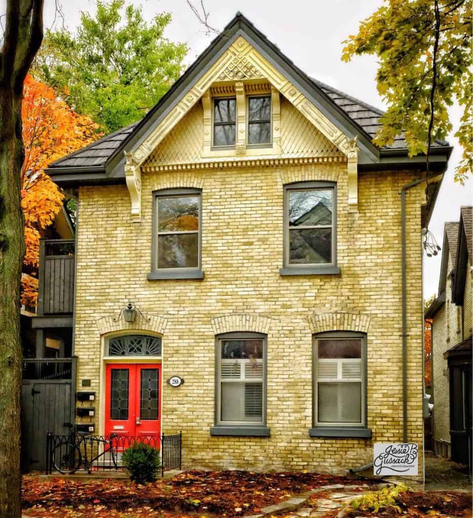 Yellow brick house with red door and autumn trees in the background.