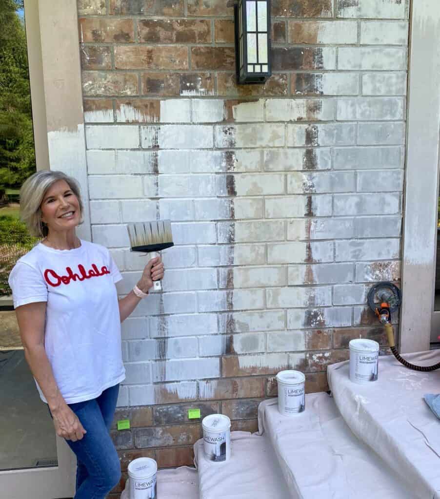 Woman painting brick wall with white paint outdoors, home improvement scene.