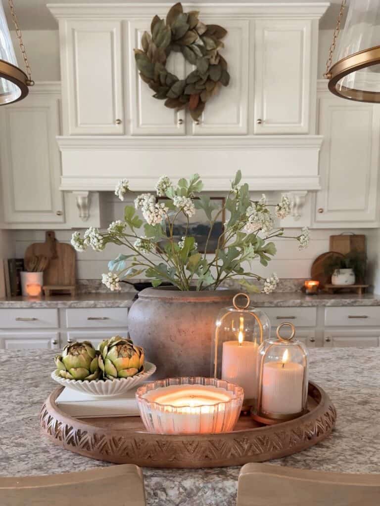 Decorative kitchen centerpiece with candles, artichokes, and floral arrangement on a tray.
