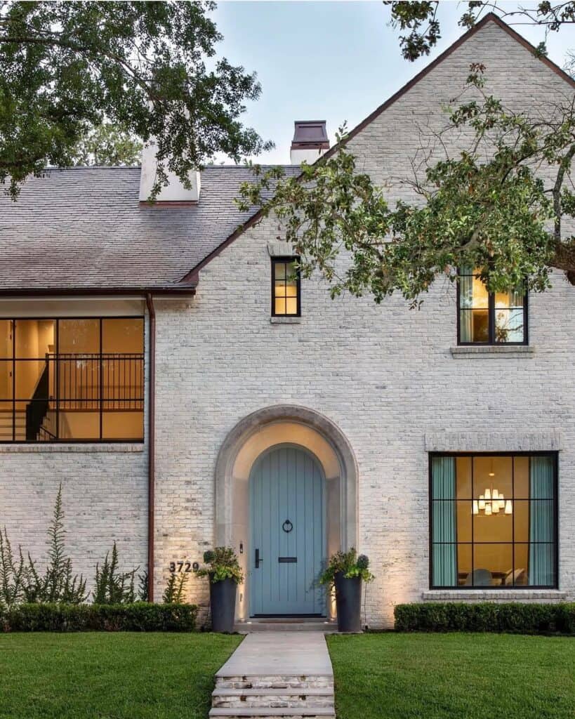 White brick house with blue door and large windows, lush front yard.