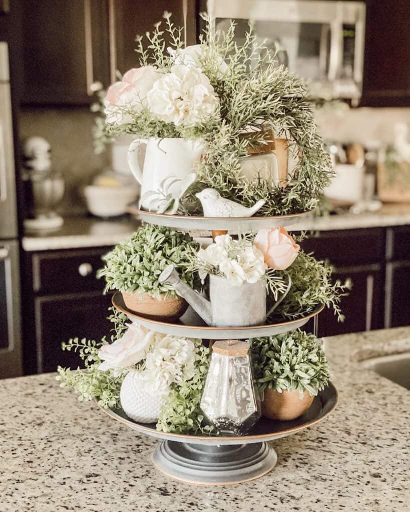 Tiered floral centerpiece with white and pink flowers in a kitchen setting.