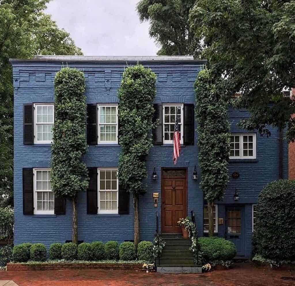 Charming blue brick house with black shutters and lush greenery.