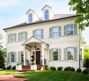 Beautiful white colonial house with front porch, lush green lawn, and mature trees.
