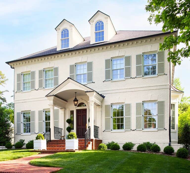 Beautiful white colonial house with front porch, lush green lawn, and mature trees.