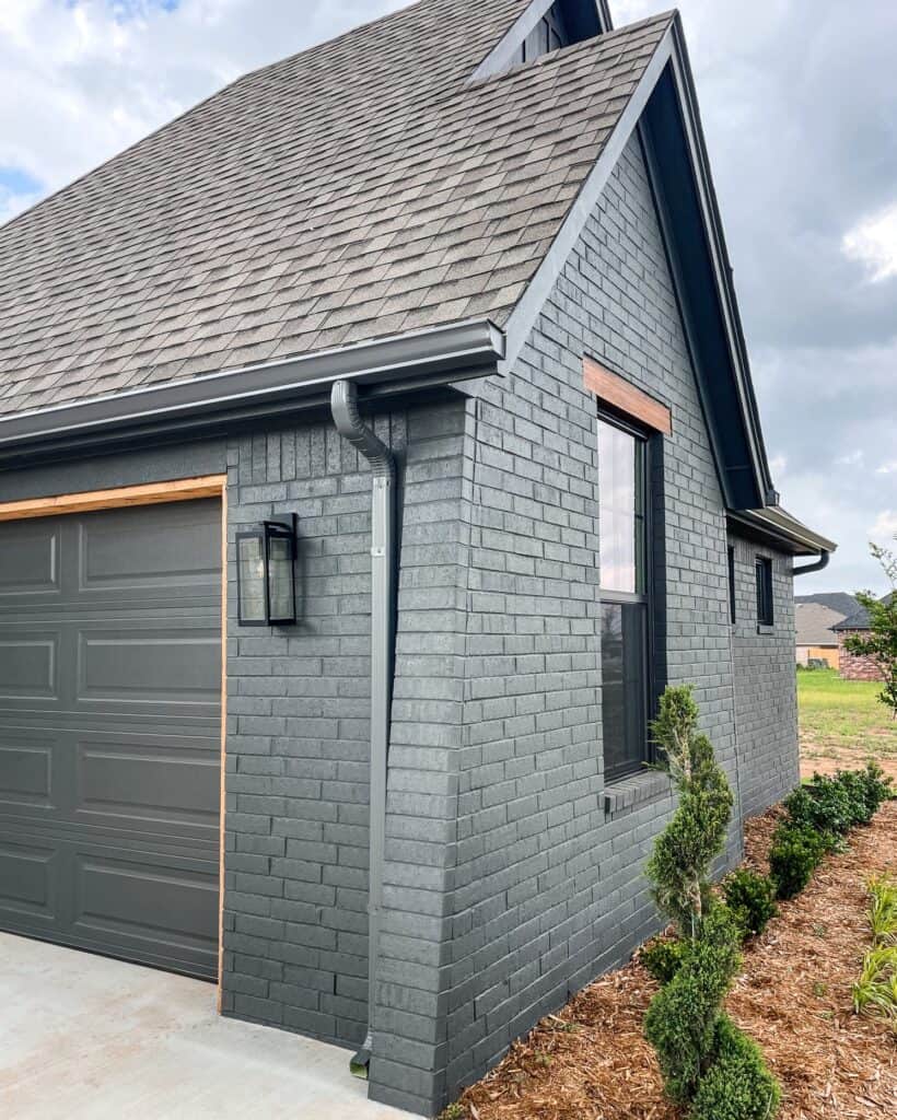 Dark gray painted brick house with black window and garage door, landscaped yard.