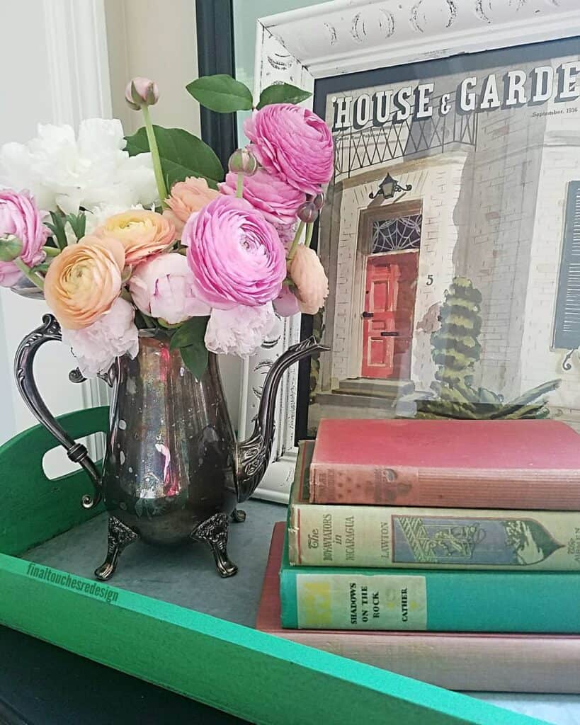 Beautiful pink and white ranunculus flowers in a vintage silver teapot on a green table.