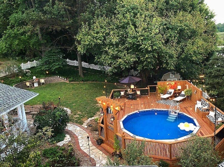 Outdoor backyard with swimming pool, wooden deck, and lush greenery.