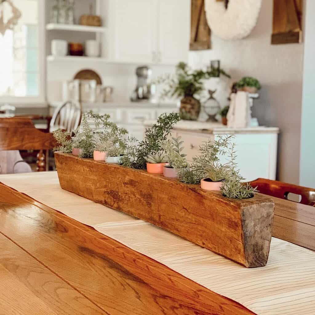 Wooden planter with succulents and greenery on kitchen table.