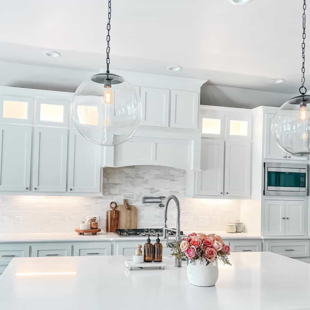 Bright white kitchen with pendant lights, marble countertops, and floral centerpiece.