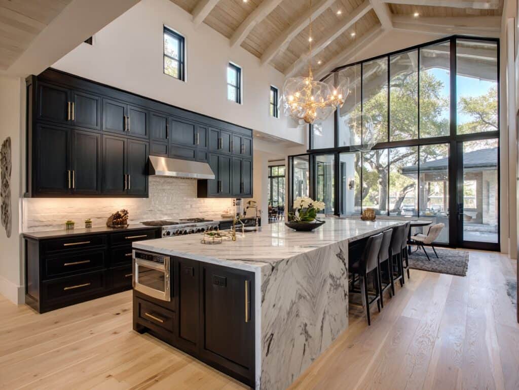 Elegant black kitchen cabinets with marble island and large windows.