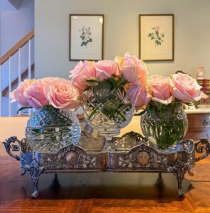 Beautiful crystal bowl with pink roses on a decorative silver tray in a cozy home setting.