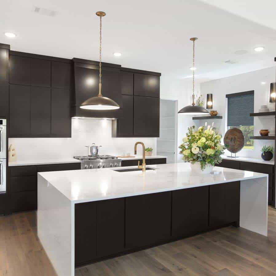 Contemporary black kitchen cabinets with white island and gold fixtures.