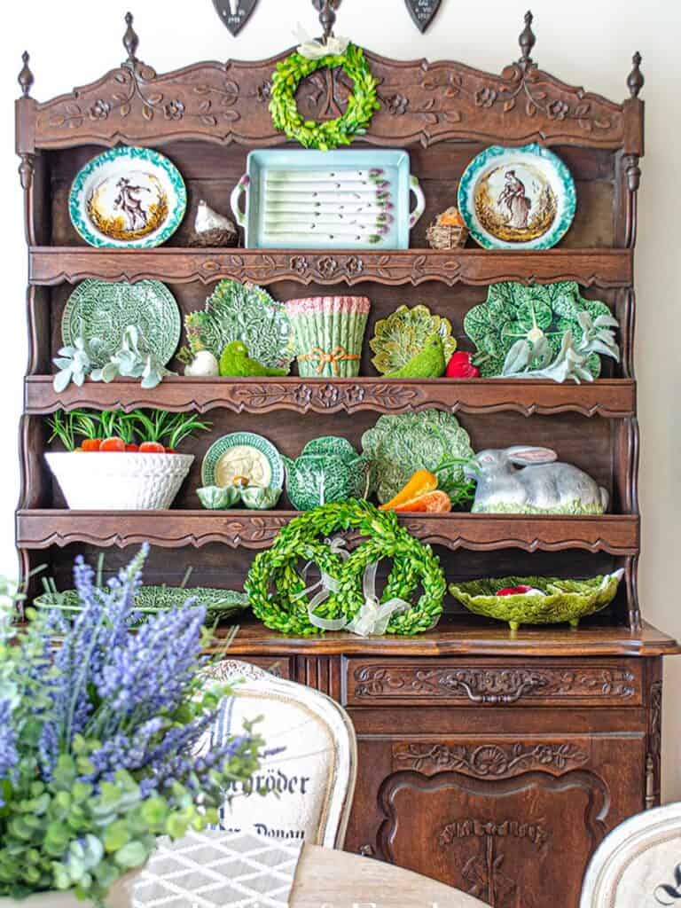 Vintage wooden hutch decorated with green wreaths, plates, and plants for home decor.