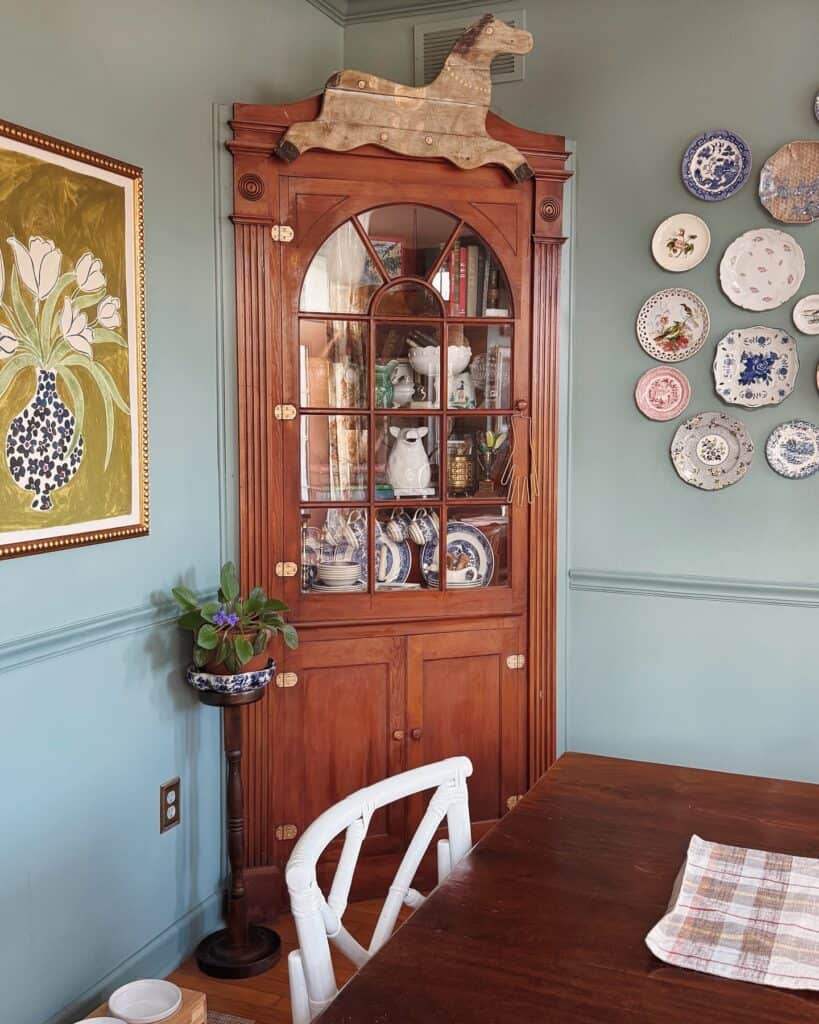 Antique wooden hutch displaying china and decorative plates in a cozy dining room.