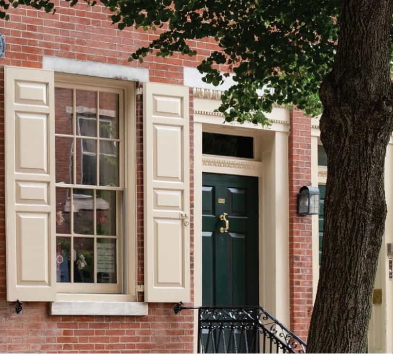 Charming brick house with green shutters and white trim, inviting entrance.