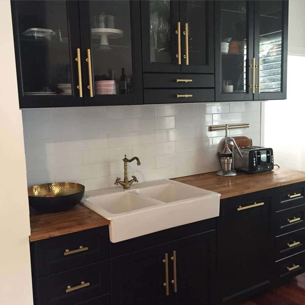 Black kitchen cabinets with gold handles and farmhouse sink in modern kitchen.