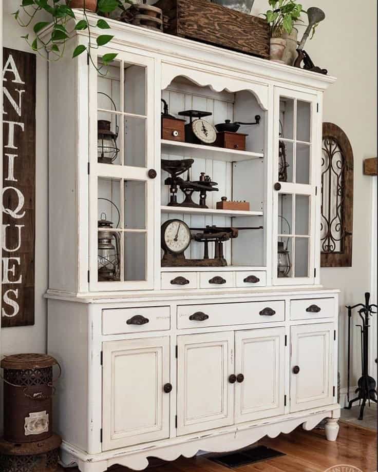 Antique white hutch with glass doors and vintage decor inside.