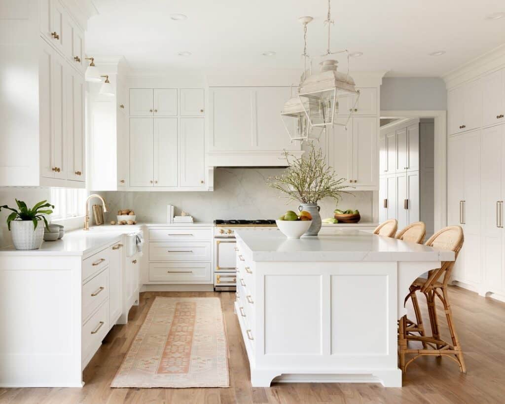 Modern white kitchen with island, barstools, and natural light.