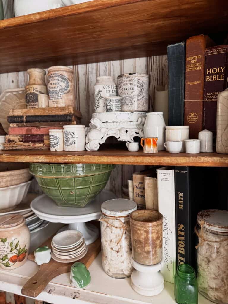 Vintage jars, books, and ceramics on a wooden hutch for home decor.