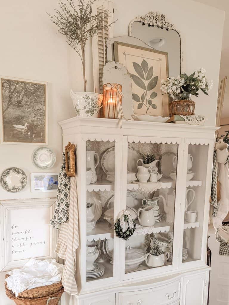 Elegant vintage white hutch with floral and greenery decor for home styling.