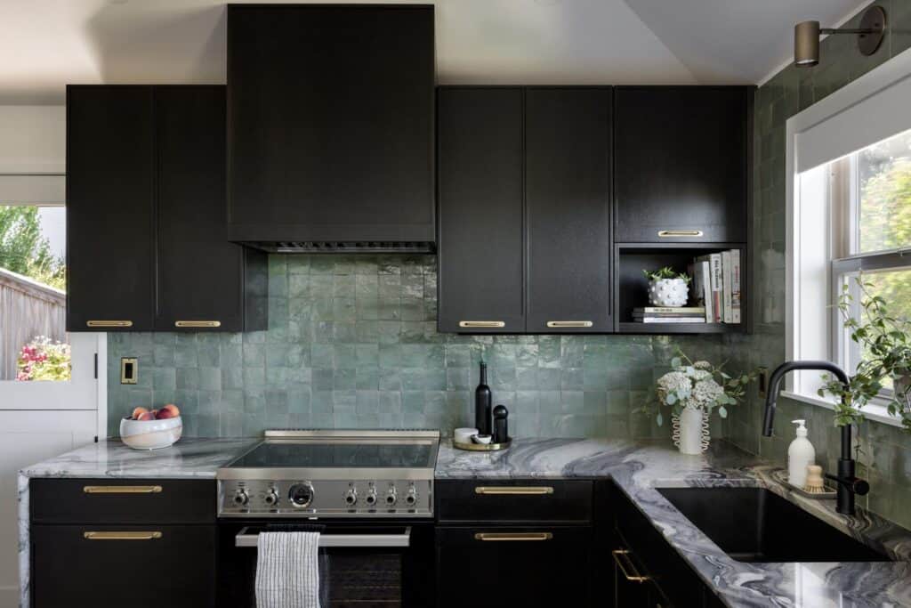 Contemporary black kitchen cabinets with green tile backsplash and marble countertop.