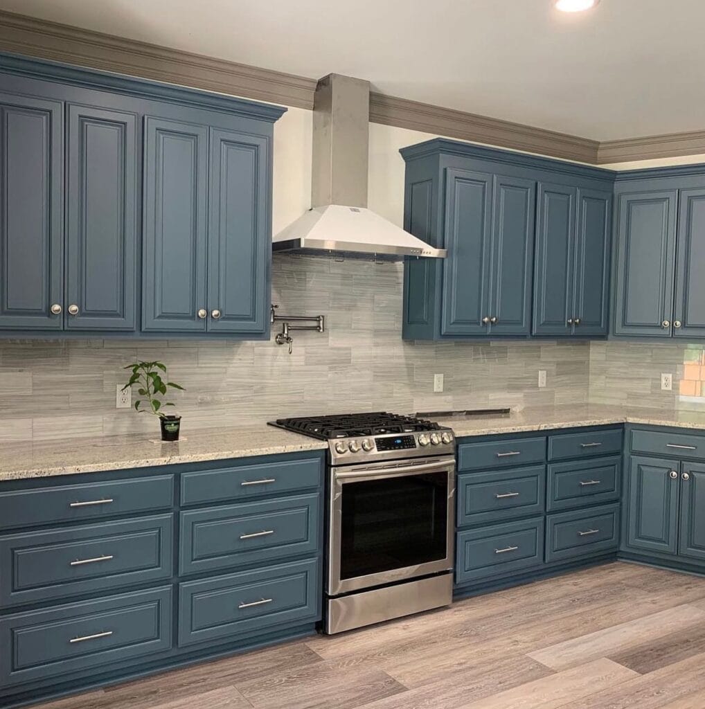 Modern kitchen with blue cabinets, stainless steel stove, and gray backsplash.