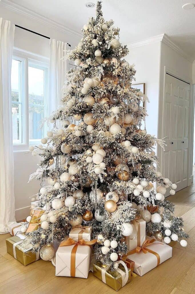 Beautiful white Christmas tree with gold and white ornaments and wrapped gifts.