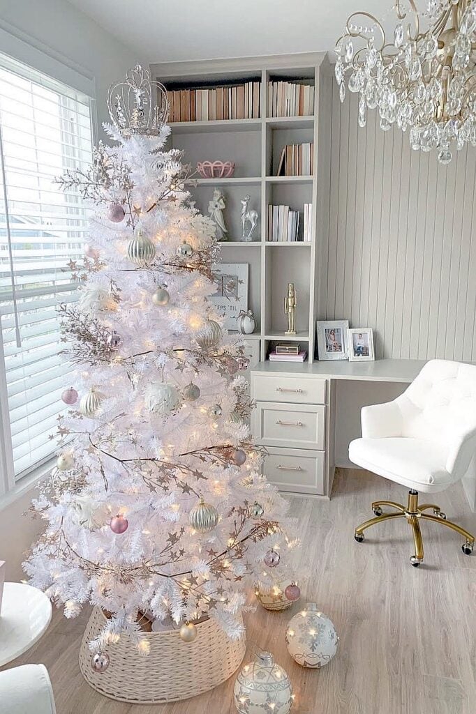 Elegant white Christmas tree with pink and gold ornaments in a bright room.
