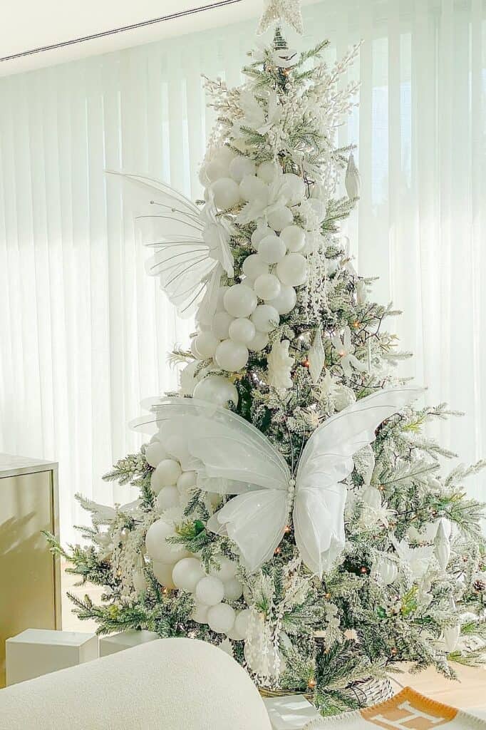 Beautiful white Christmas tree with butterflies and ornaments in a bright room.
