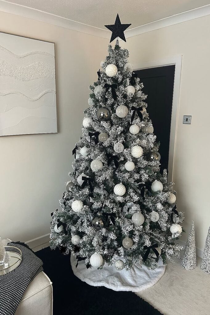 Beautiful white Christmas tree with silver ornaments and star topper in living room.