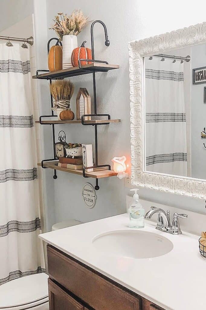 Decorative bathroom with wall shelves, pumpkins, and a white sink for fall decor.