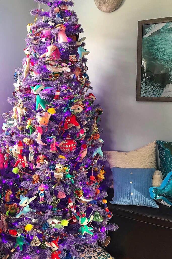 Decorated purple Christmas tree with colorful ornaments and lights in living room.