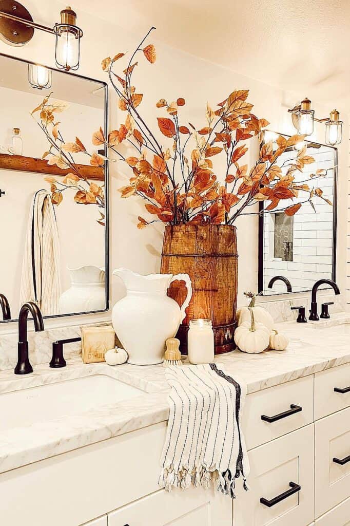 Decorative autumn leaves in a wooden vase on bathroom counter with pumpkins and towels.