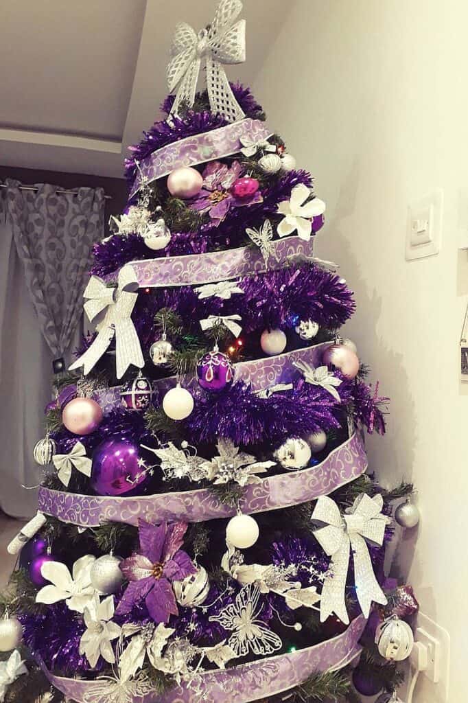 Decorated purple Christmas tree with white and silver ornaments and ribbons.