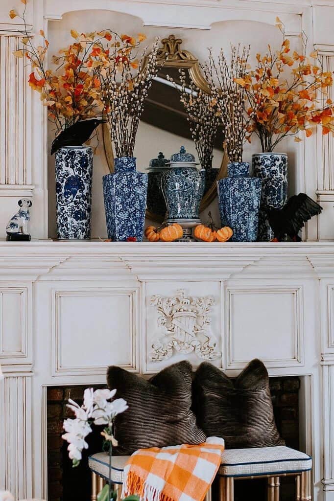 Fall decor on fireplace mantel with blue vases, orange leaves, and pumpkins.