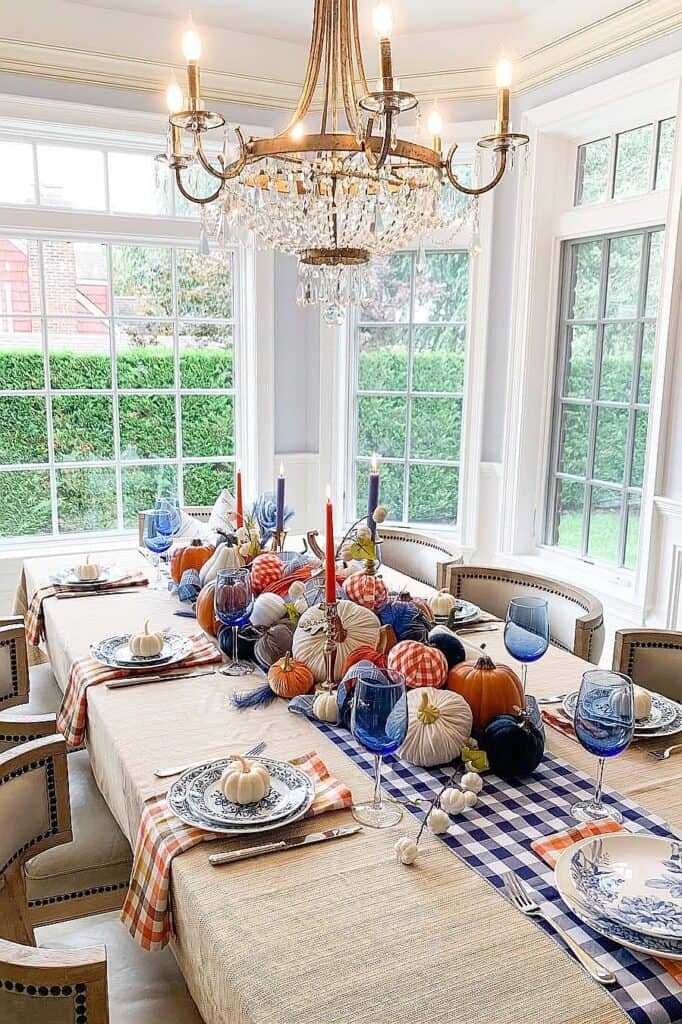 Elegant fall table setting with pumpkins, candles, and blue glasses for autumn decor.