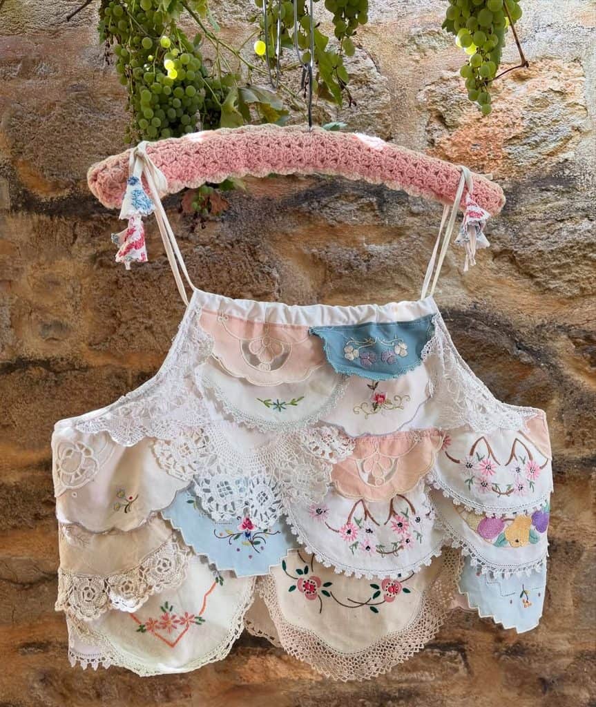 Colorful vintage doily skirt hanging on a pink crochet hanger against a stone wall.