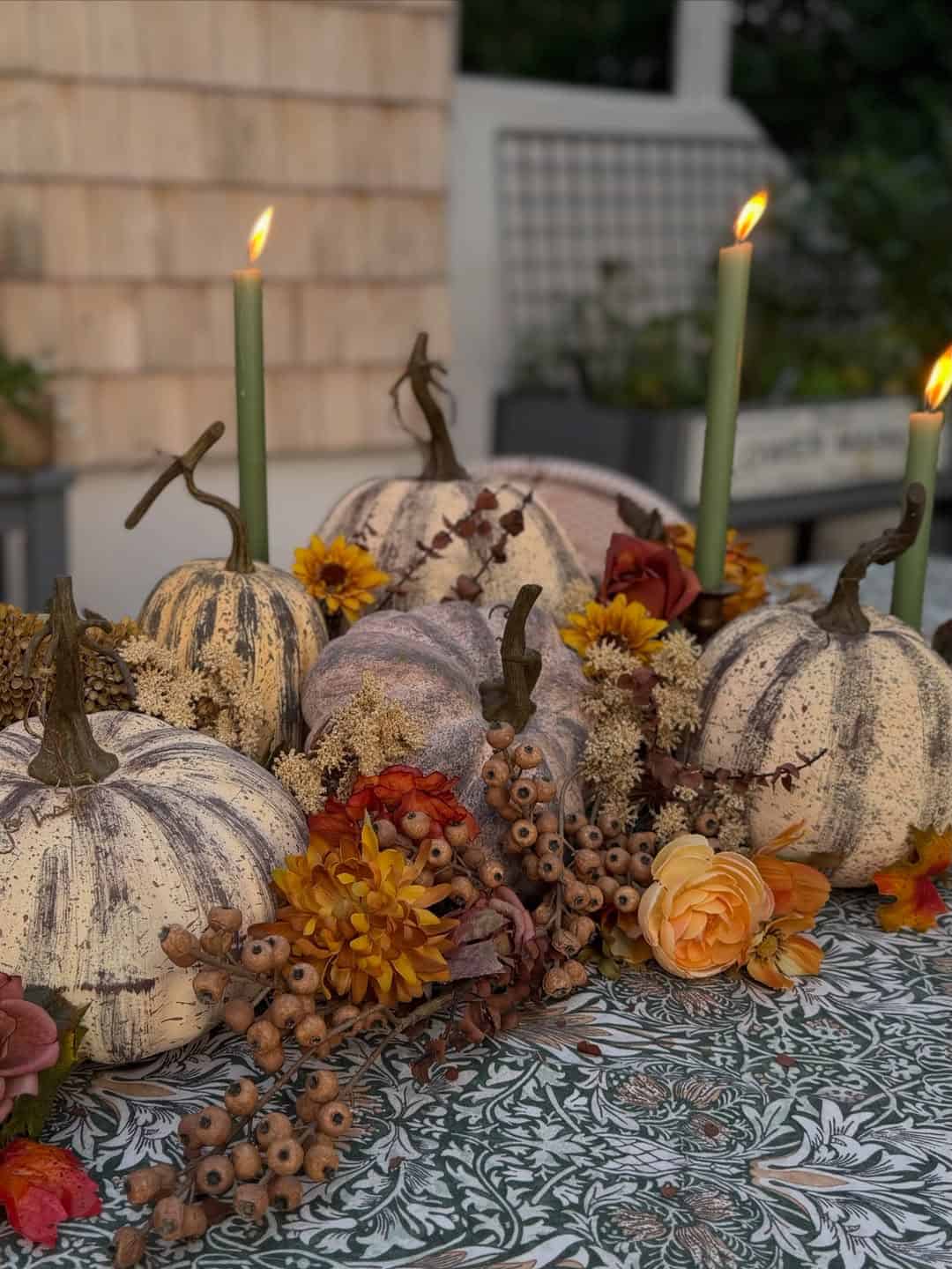 Fall pumpkin centerpiece with candles, flowers, and berries for autumn decor.