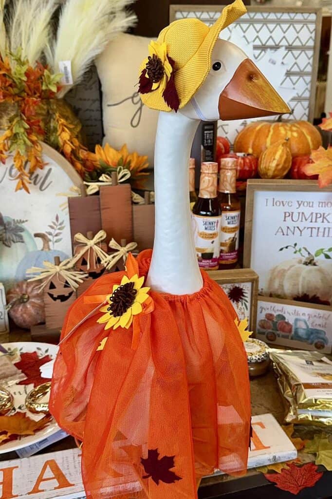 Decorative goose with yellow hat and orange tutu for fall porch decor.