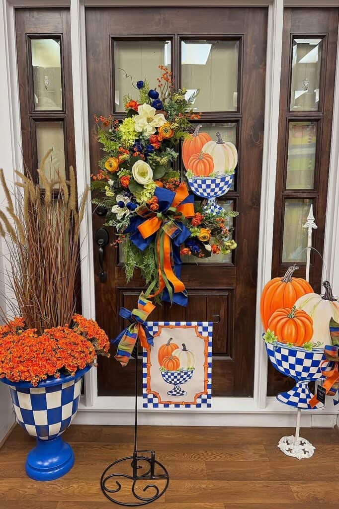 Colorful fall floral arrangement with pumpkins and orange-blue ribbons on front door.