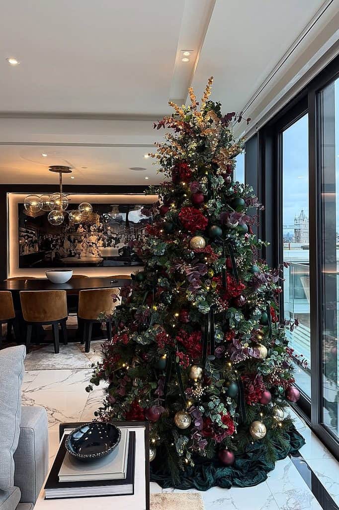 Beautifully decorated Christmas tree with burgundy, gold, and silver ornaments in a modern living.