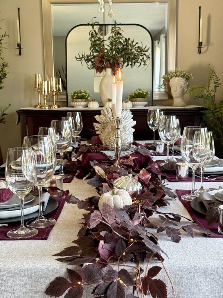 Fall-themed dining table with pumpkins, leaves, candles, and floral centerpiece.