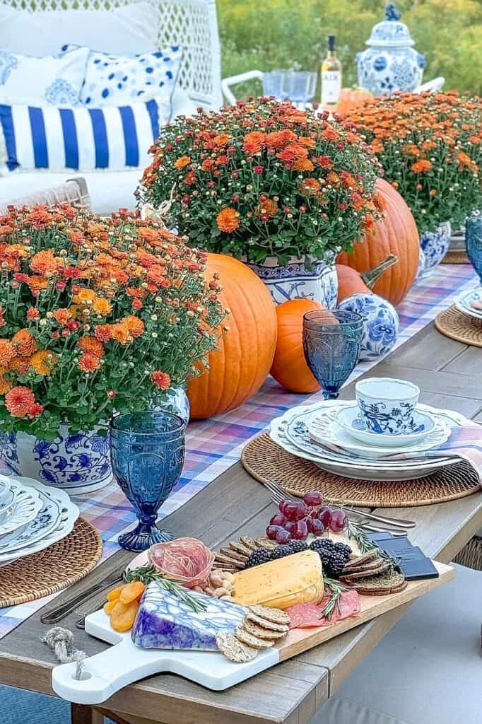 Outdoor fall table setting with pumpkins, orange flowers, and blue accents.