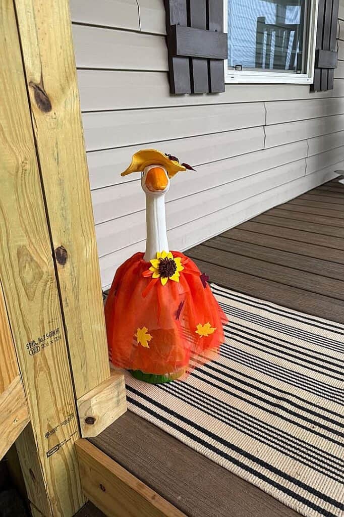 Decorative goose with fall-themed tutu and sunflower on porch.