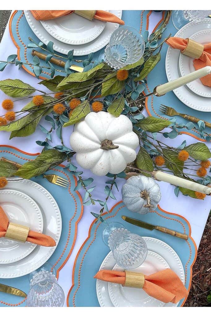 Elegant fall table setting with white pumpkins, orange accents, and greenery.