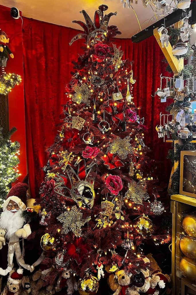 Festive Christmas tree decorated with red, gold, and glittering ornaments in a cozy room.