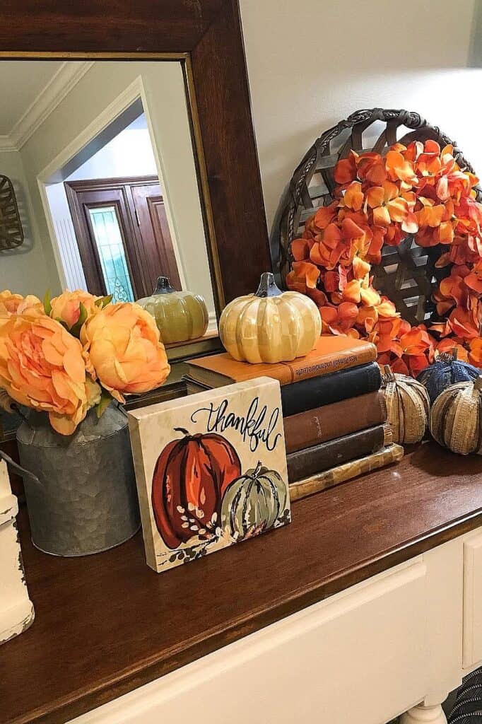 Autumn-themed fall decor with pumpkins, wreath, and thankful sign on a wooden table.